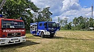 Auf einem Sportplatz steht ein blaues Fahrzeug des Technischen Hilfswerkes neben einem roten Fahrzeug der Feuerwehr.